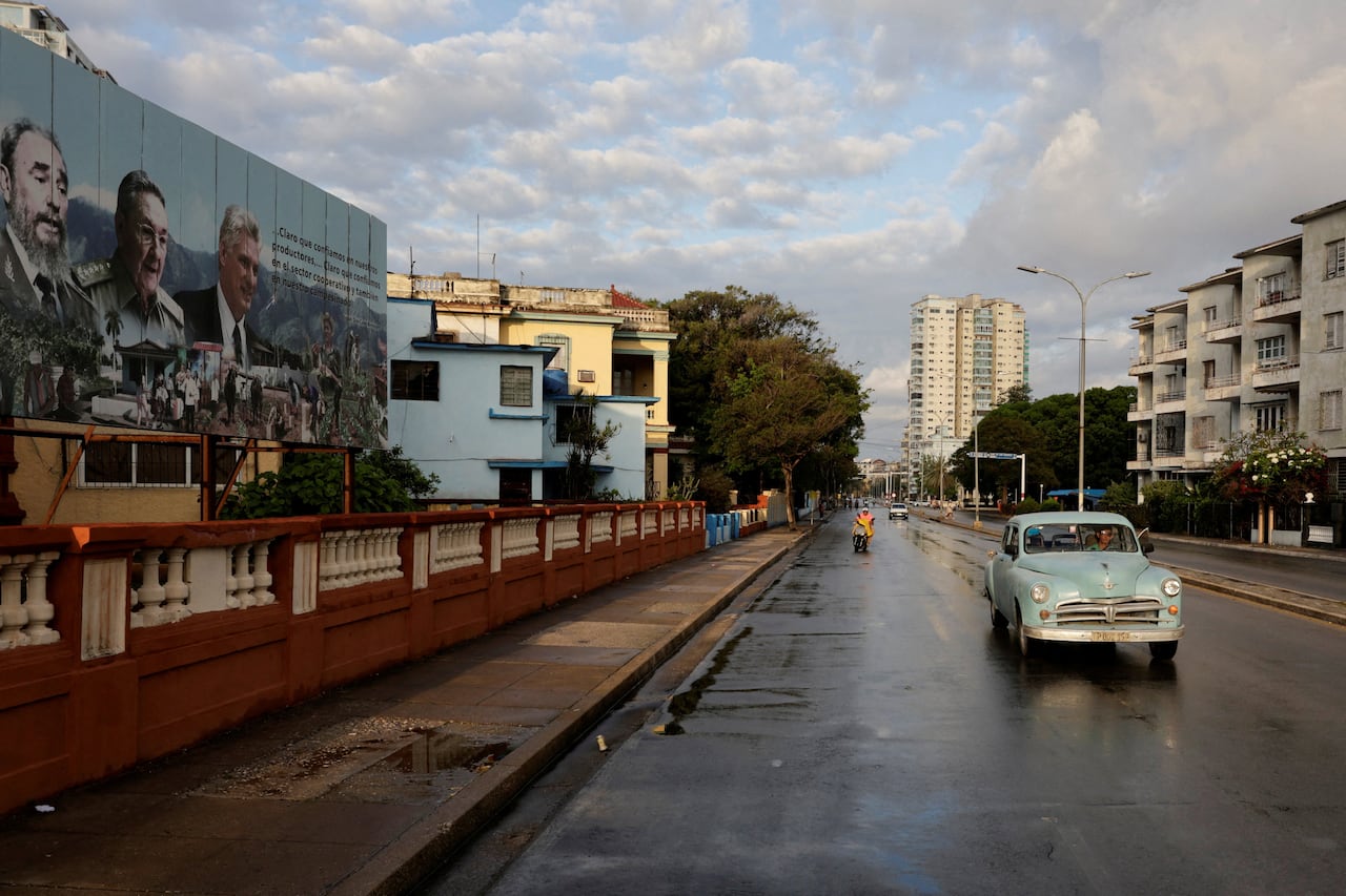 A classic car drives down a street in Havana, near a billboard showing images of Fidel Castro, Raul Castro and Miguel Diaz-Canel.