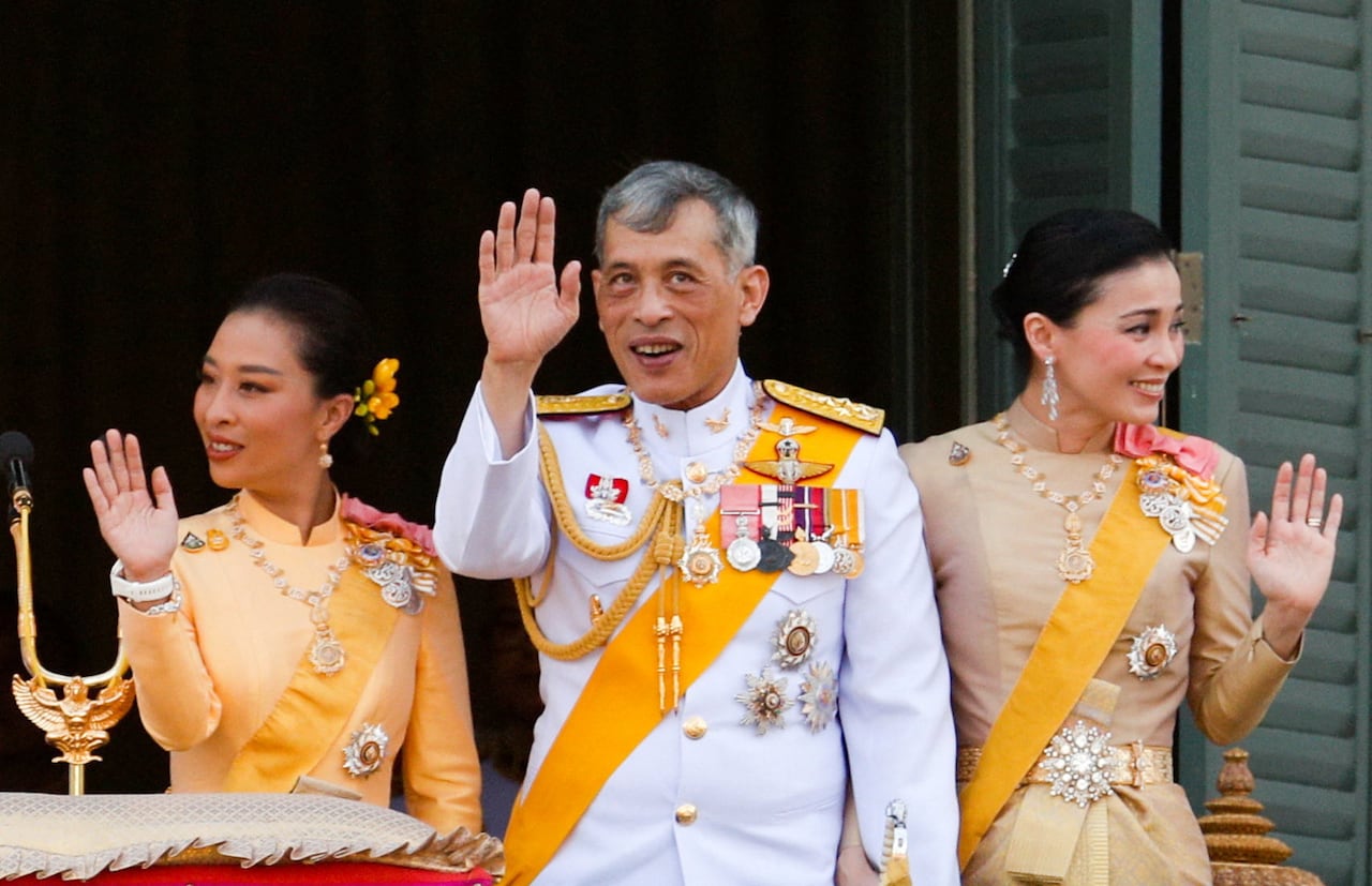 Two women and a man wave from a balcony.