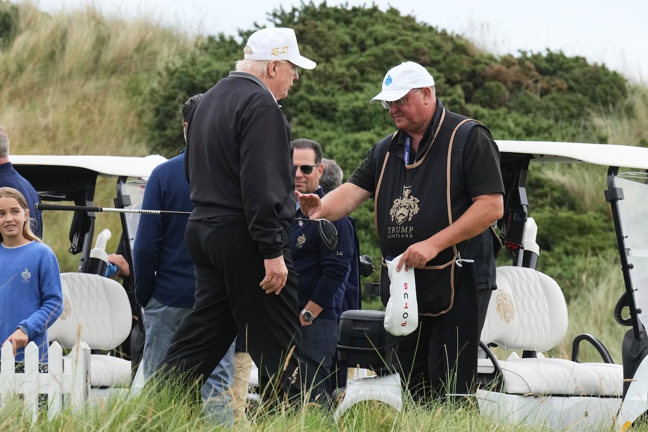 Donald Trump hands a golf club to a caddie.