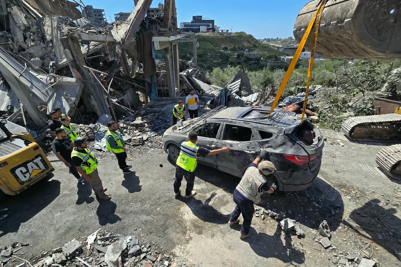 Workers tow a damaged car amongst the rubble.