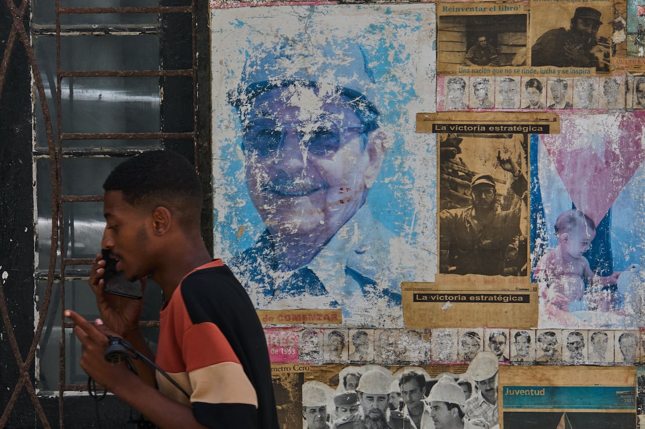 A man talks on a cellphone, while in the vicinity of images of Raúl and Fidel Castro displayed at a building in Havana.