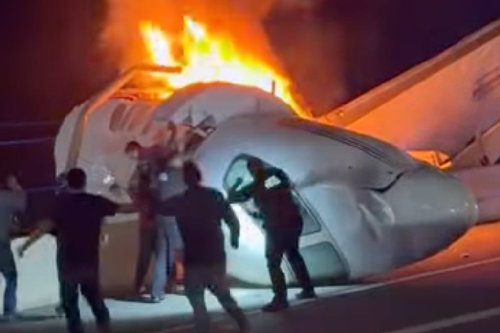 A passenger jumps out of a plane after it crashed on a highway as other people help.