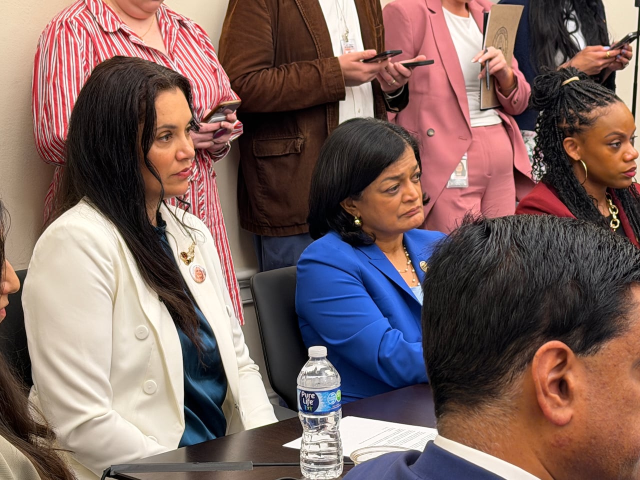 Two women with dark hair wearing blazers sit in a crowded meeting room.
