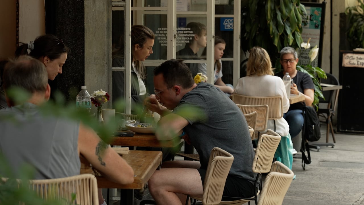 People eating at tables along a sidewalk patio in summer clothes.