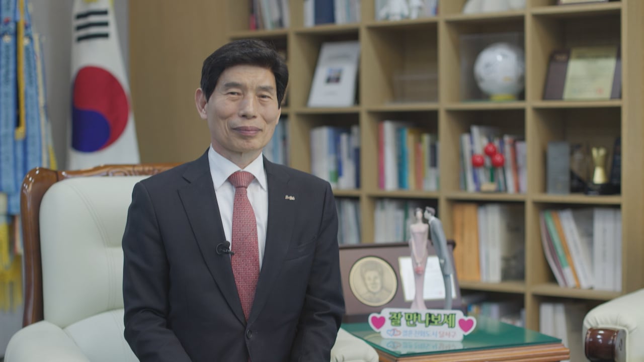 A man in a suit looks at the camera. There is a South Korean flag behind him