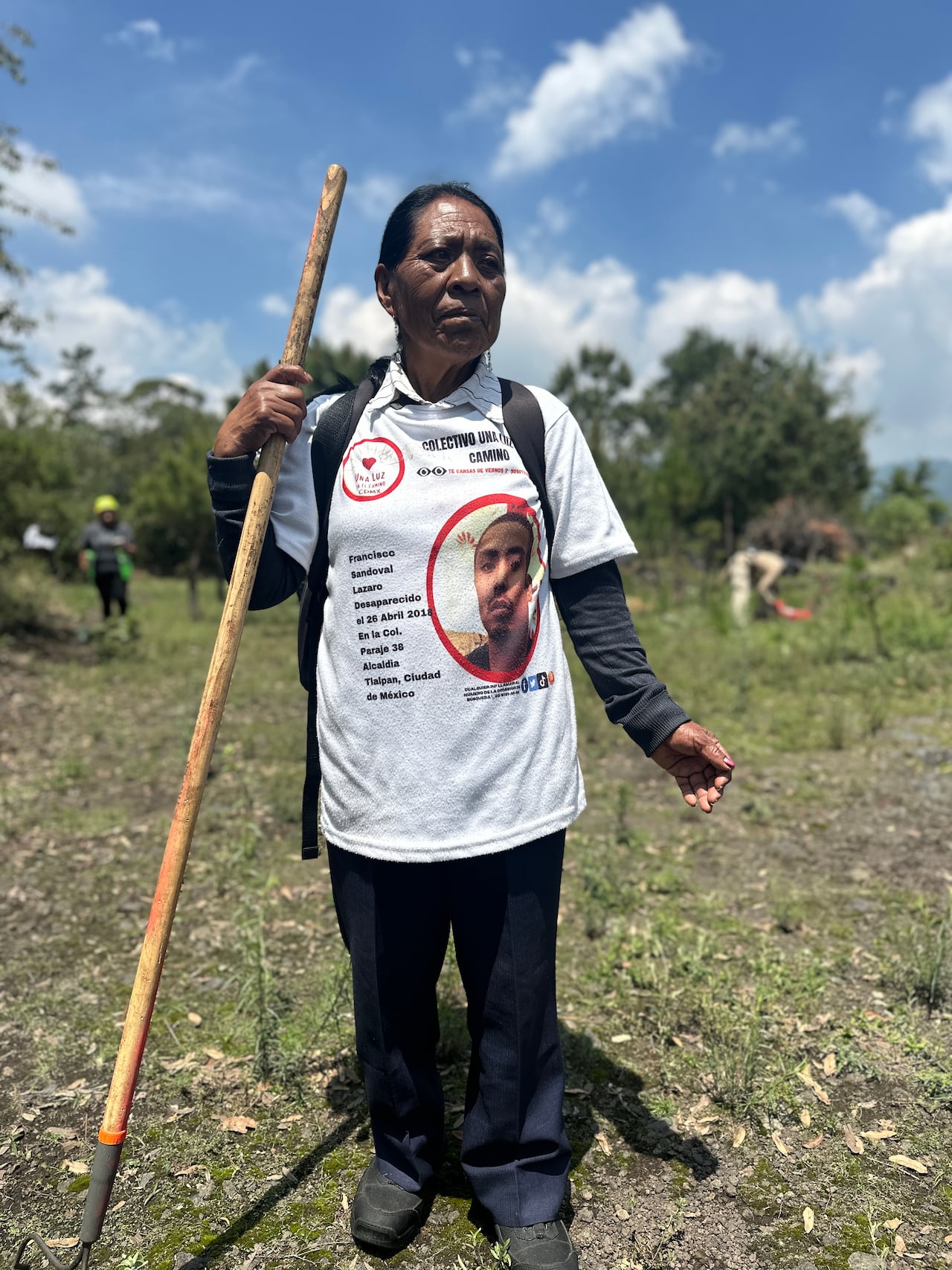 A woman stands holding a rake in her left hand.