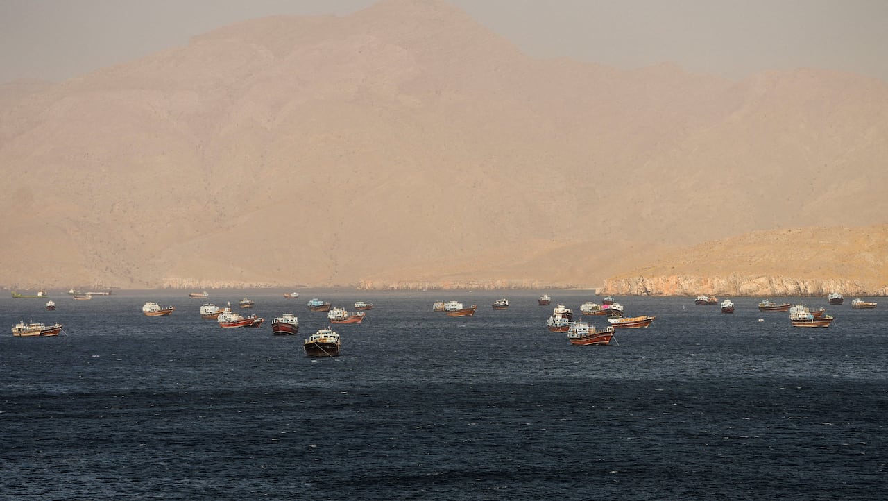 Small boats are seen anchored at sea with tan-coloured hills in the background.