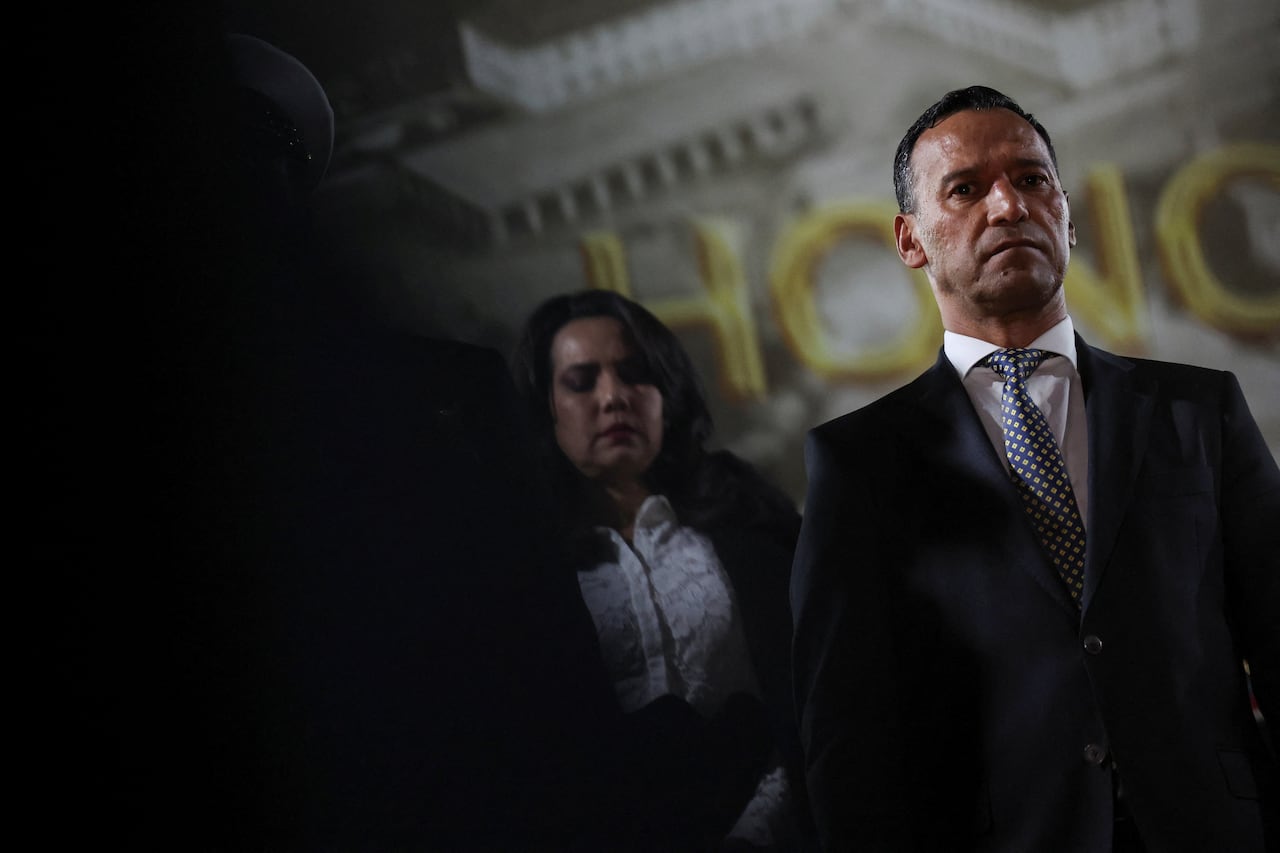 A man stands to the right of the frame with shadows in the background.
