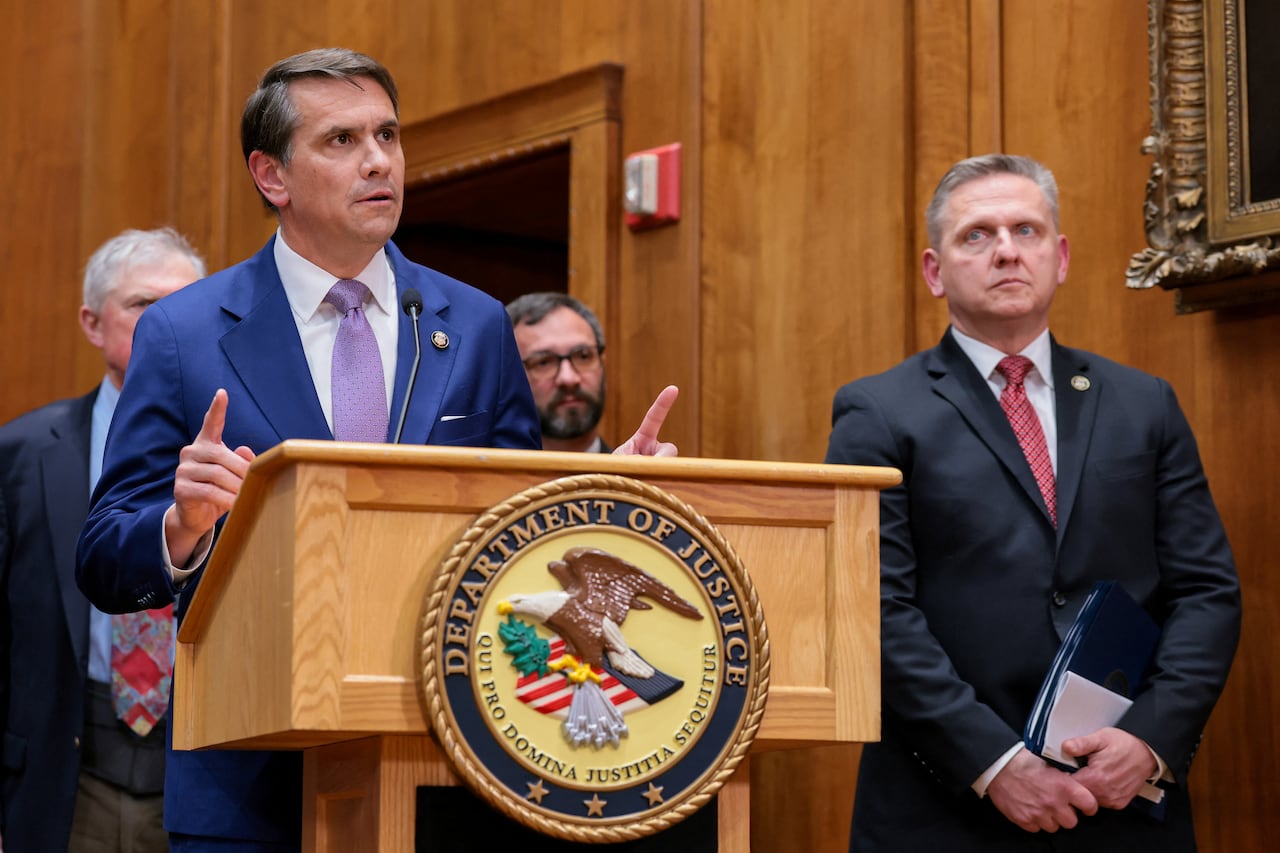 Two men, one behind a podium, stand and speak to a room