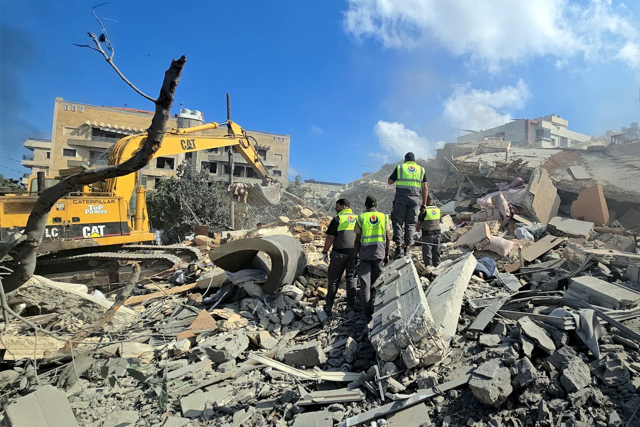 Civil defence workers stand on top of rubble.