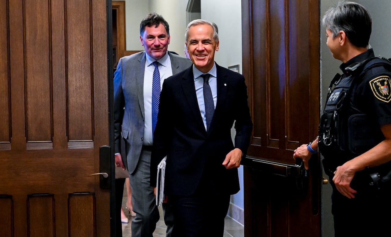 Mark Carney walks past a door held open by a parliamentary protective service officer, with Dominic LeBlanc walking behind him.