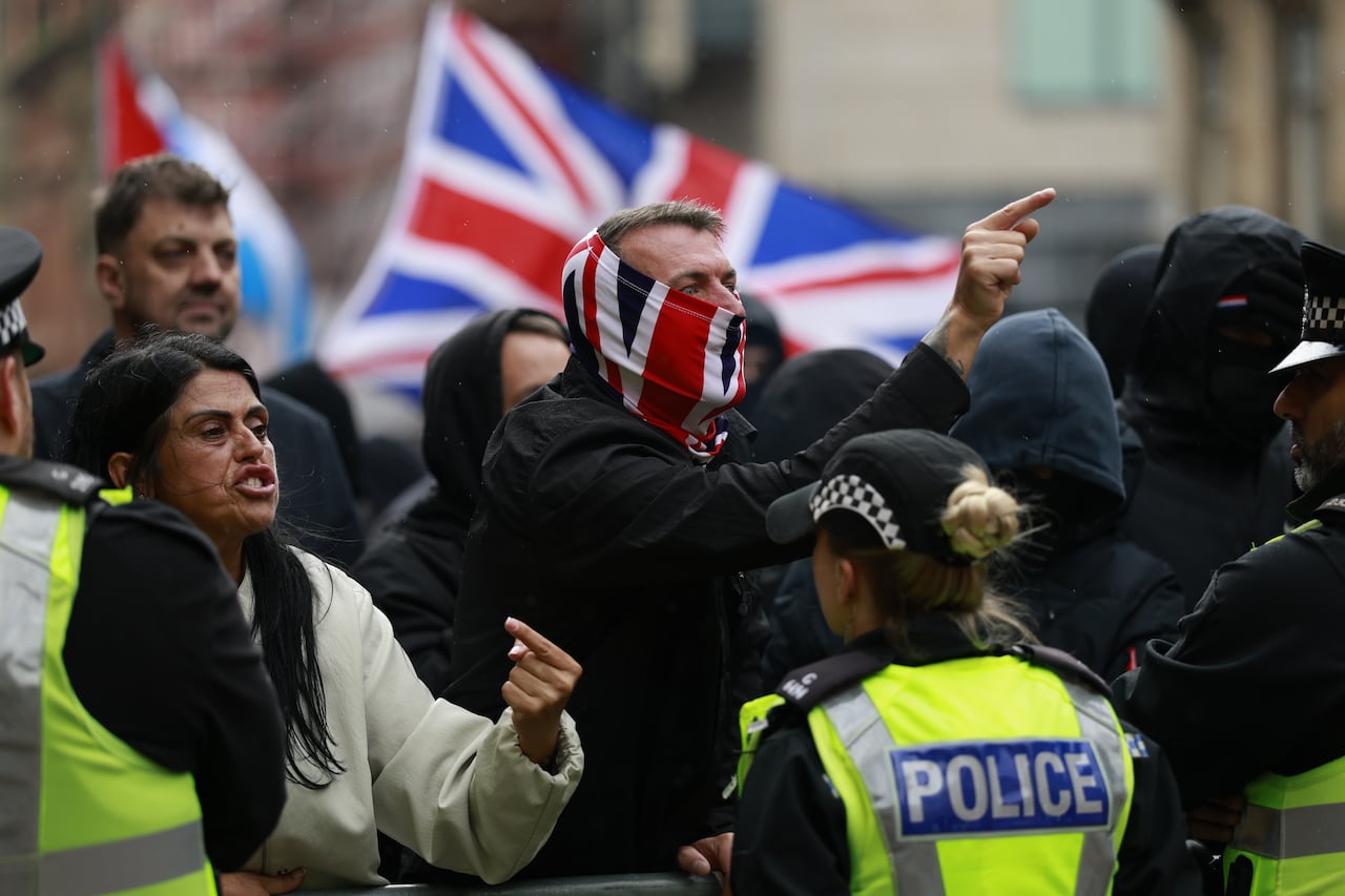 Protesters yell and shout behind a line of police officers.