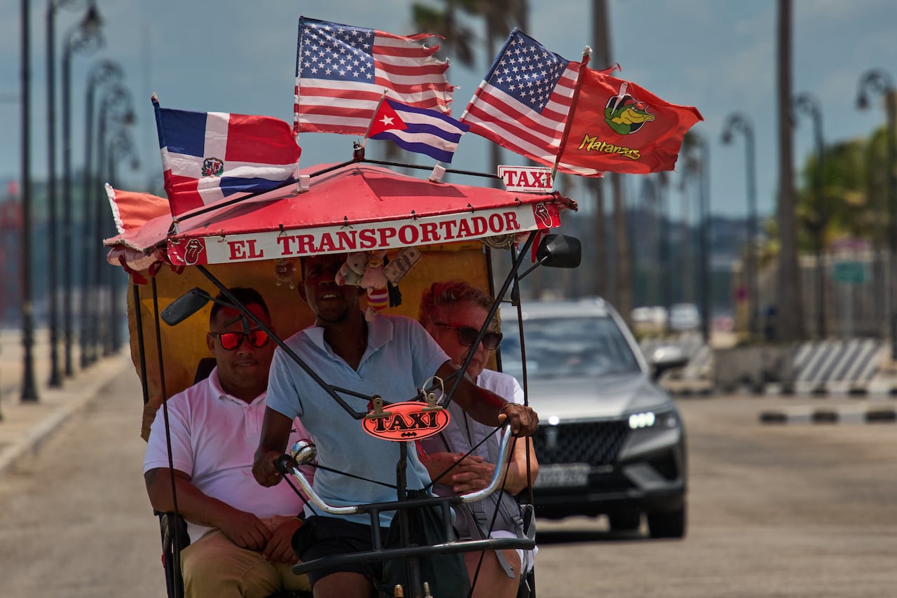A man pedals a bicycle taxi, carrying two passengers, in Havana, Cuba.