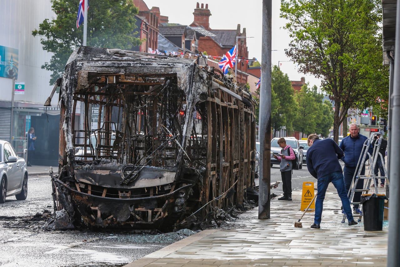 A burned and hallowed out bus is shown on a city street.