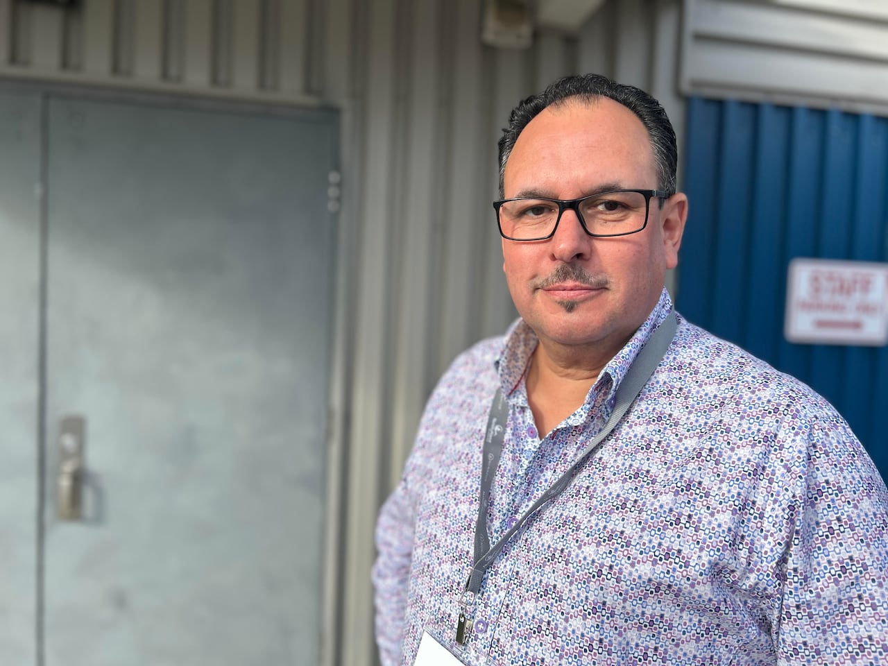 A man wearing glasses and a purple print shirt poses in front of a door.
