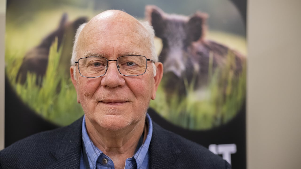 A man stands in front of a photo of wild pigs.