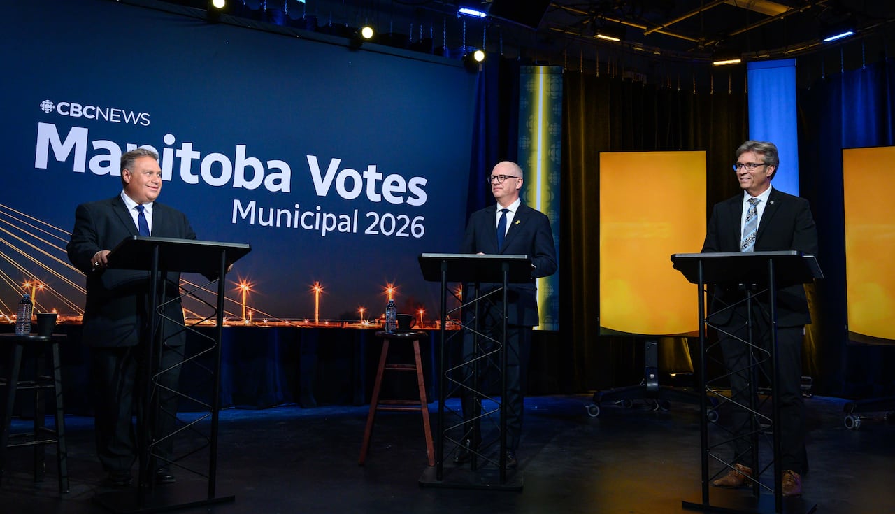 Three people stand behind podiums on a lit stage.