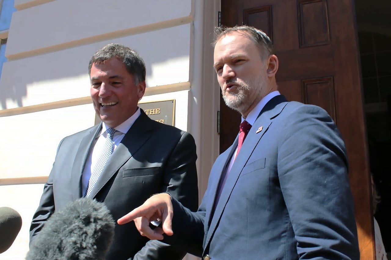 Two men in suits speak to reporters.