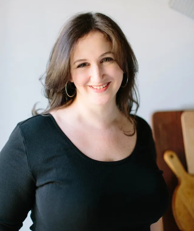 A woman with dark hair in a black shirt smiles at the kitchen