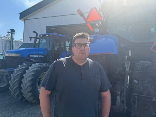 President of a faming association in dark blue shirt stands infront of a tractor