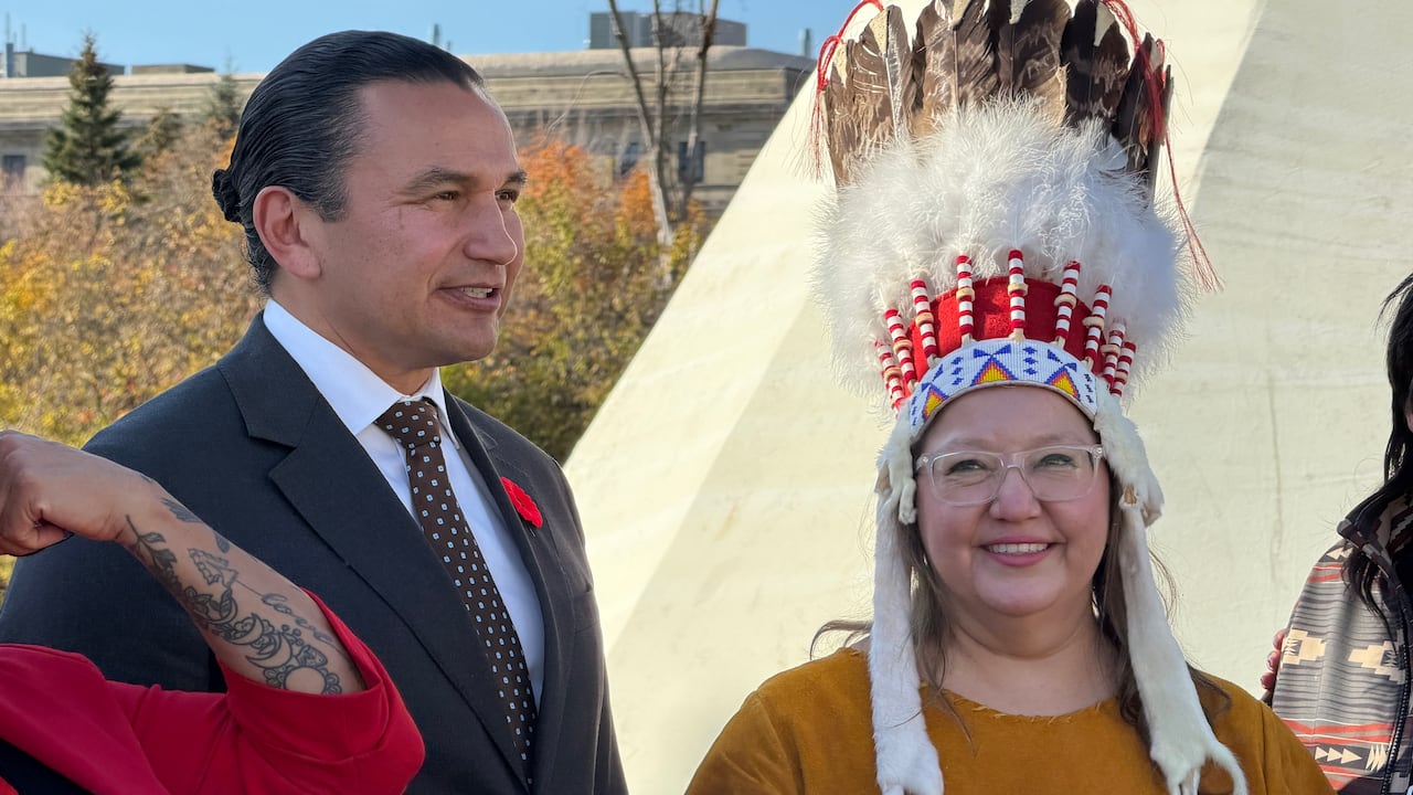 Two people stand for a photo with a teepee behind them.