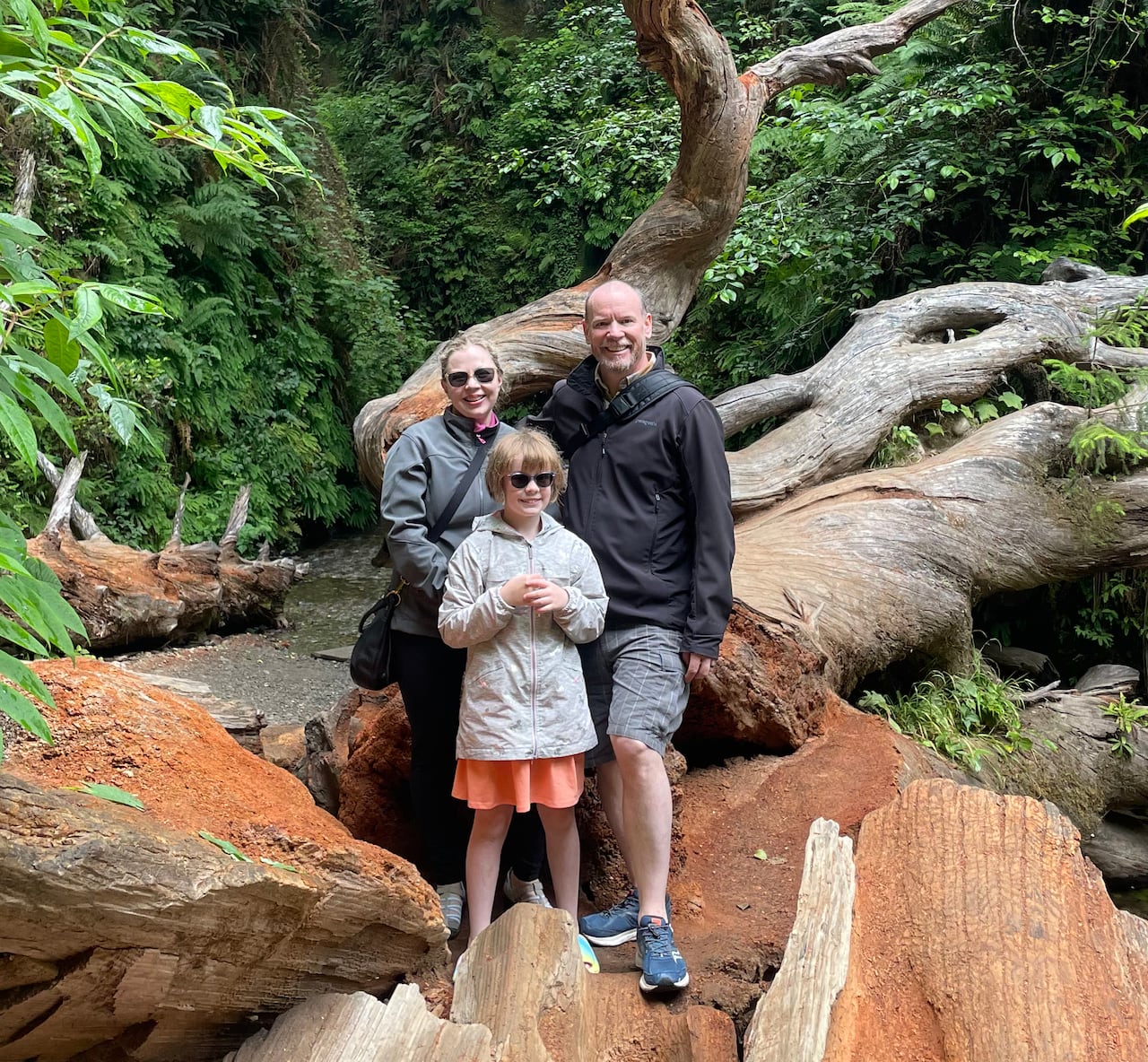 A woman, young girl and man standing together on a red rock in a forest