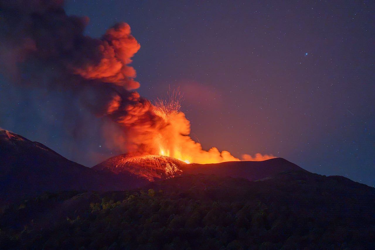 Smoke and red-orange lava spewing from the crater of an active volcano at dusk or dawn.