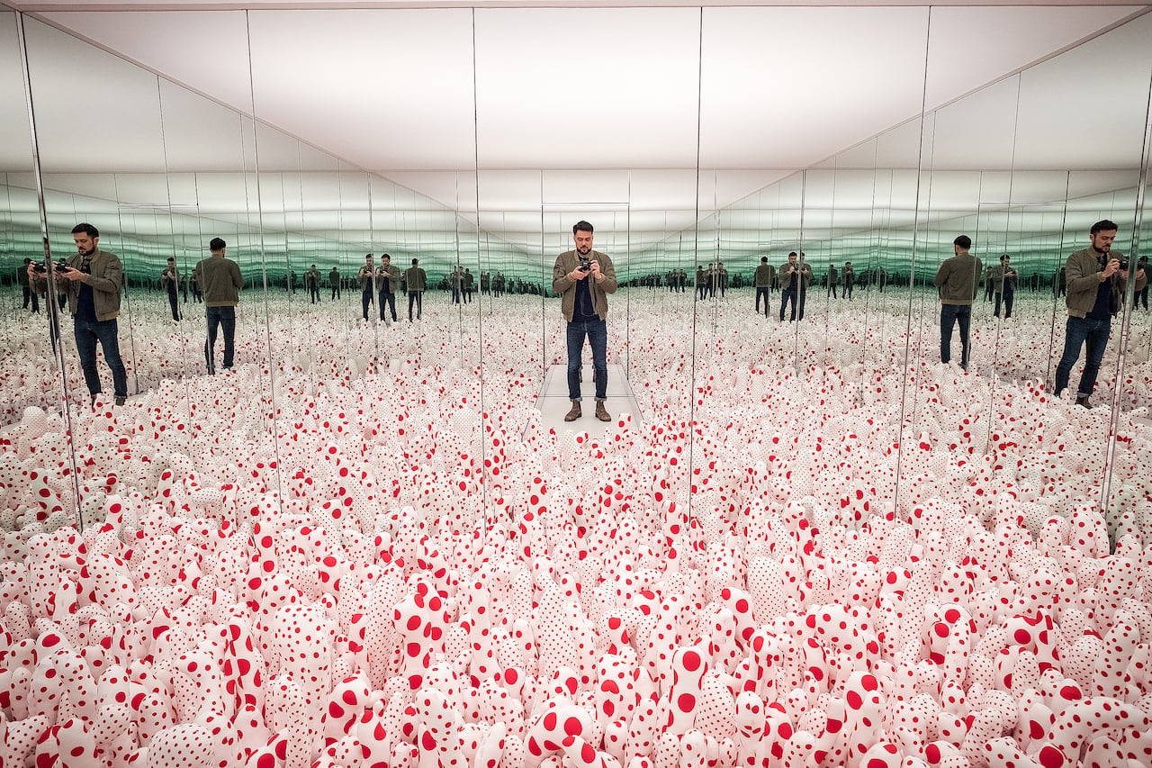 A picture of a man standing in an art installation taking a picture of his reflection in the mirror