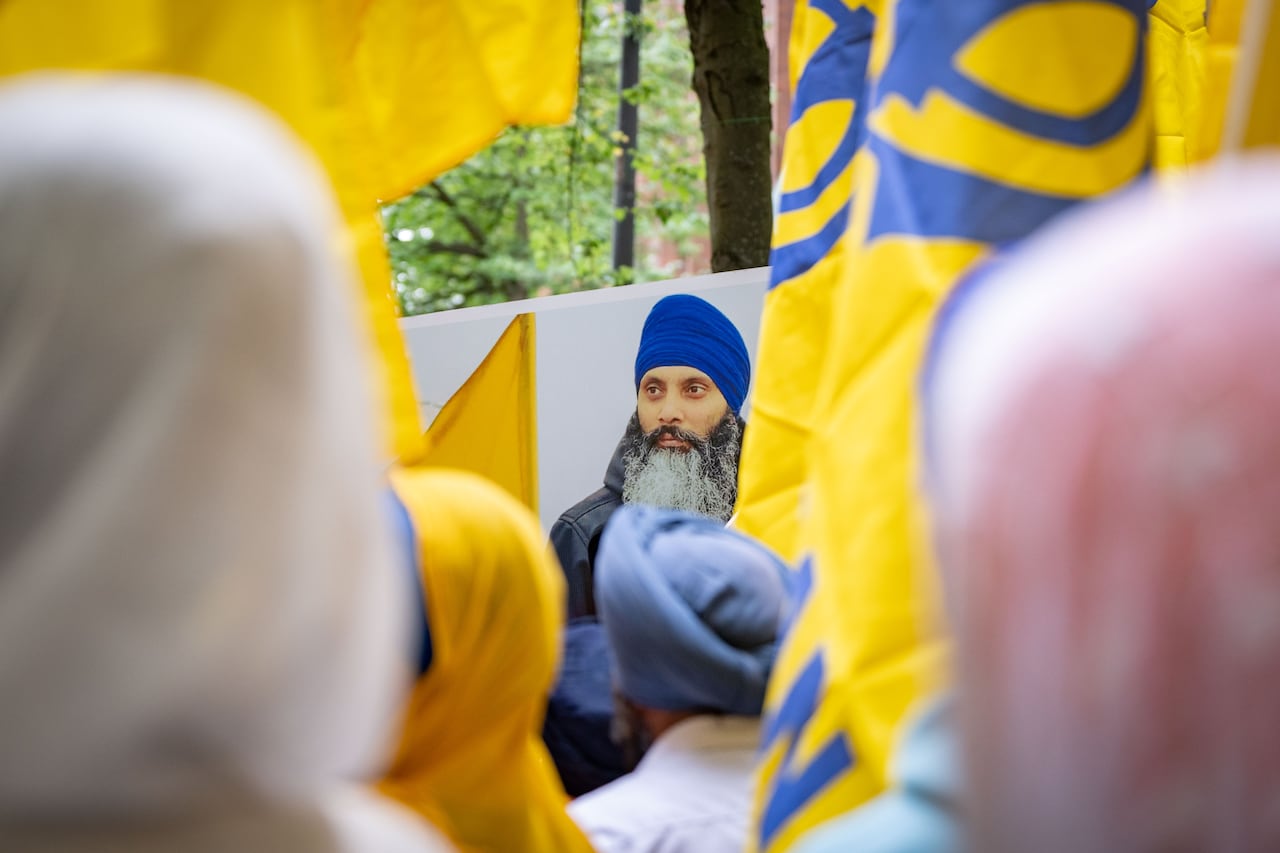 People wearing head coverings stand in front of a bearded man wearing a blue turban.