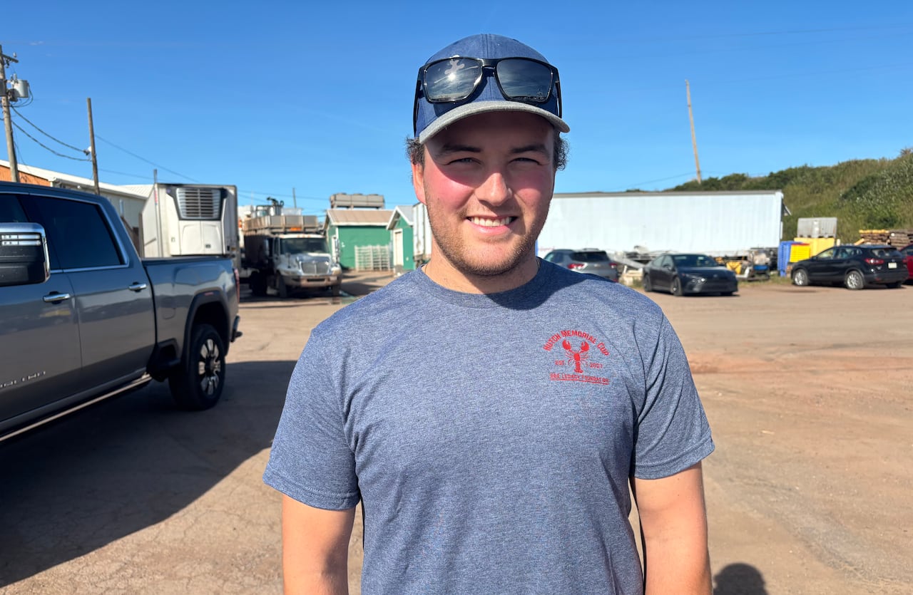 A man wearing a blue shirt and baseball cap smiling in a car park at a fishing wharf