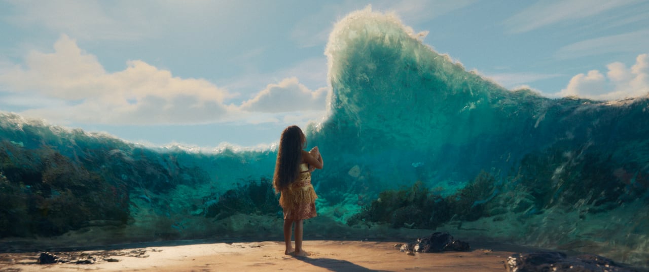 A CGI image shows a woman standing on a beach. In front of her, a large blob of water rises out of the ocean and hovers above her.