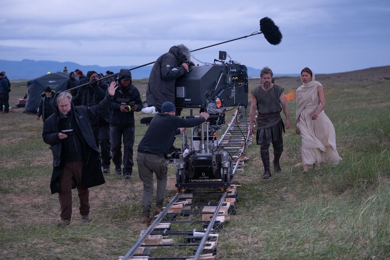 A director and a film crew shoot footage of two actors on a hill dressed in ancient clothes.