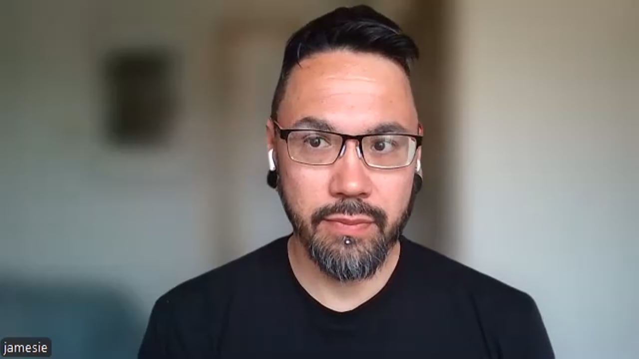 A man wearing glasses and a black t-shirt with earbuds in.