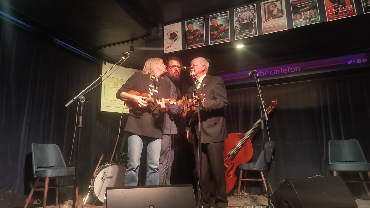 a woman and two men playing the ukulele together and singing.