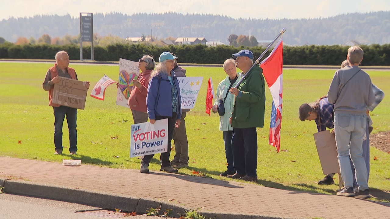 A group of advocates for Canada-U.S. relations are pictured holding up signs at the Peace Arch border crossing.
