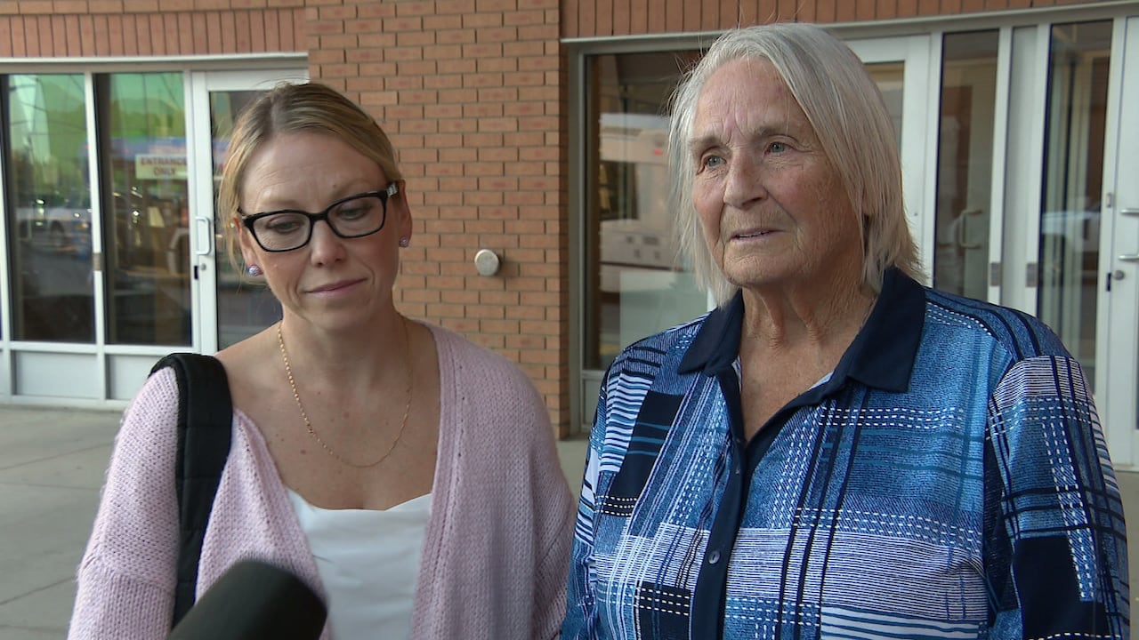 Two women look sad, standing outside of a courthouse.