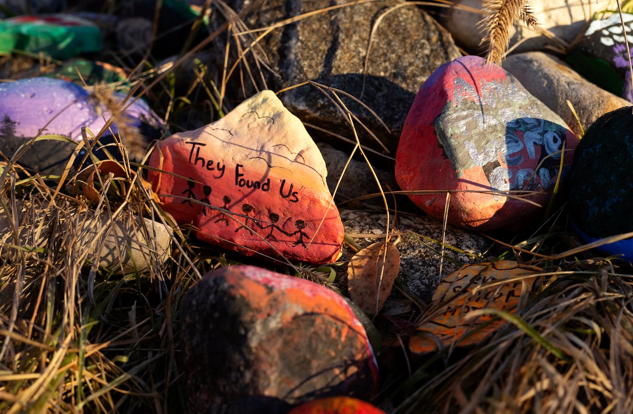 Rocks painted with the words they found us sit among a pile of other painted rocks in the fall.
