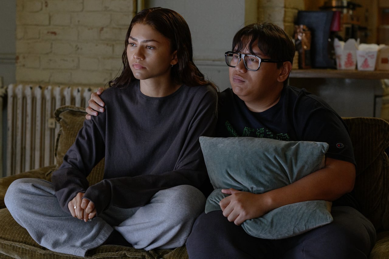The actors Zendaya and Jacob Batalon as MJ and Ned sit on a couch.
