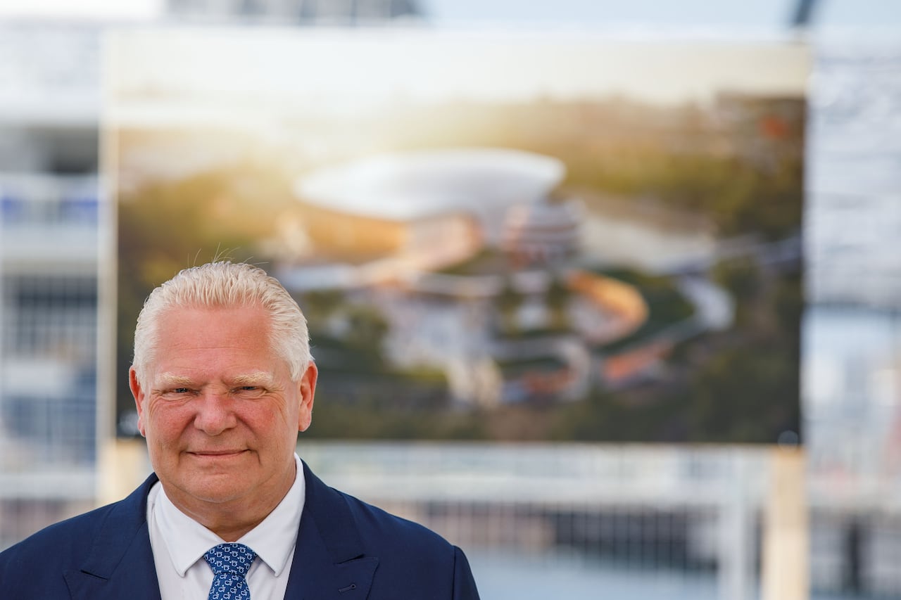 Ontario Premier Doug Ford standing in front of a printed out rendering of Ontario Place. 