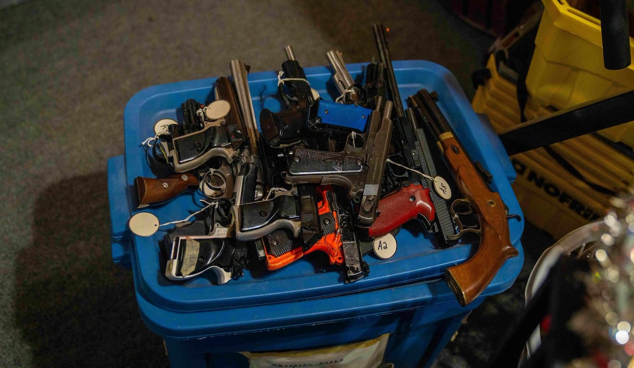 Numerous handguns are seen stacked on a plastic container.