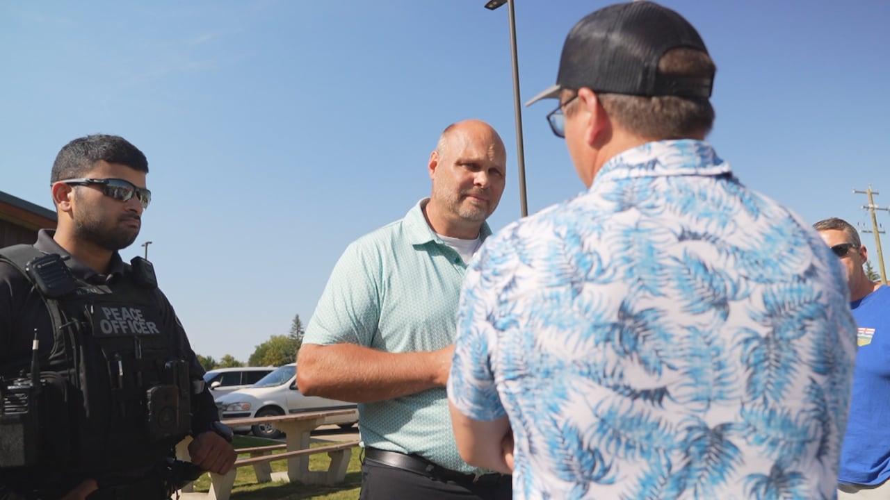 A man and a police officer speak to a man wearing a hat.