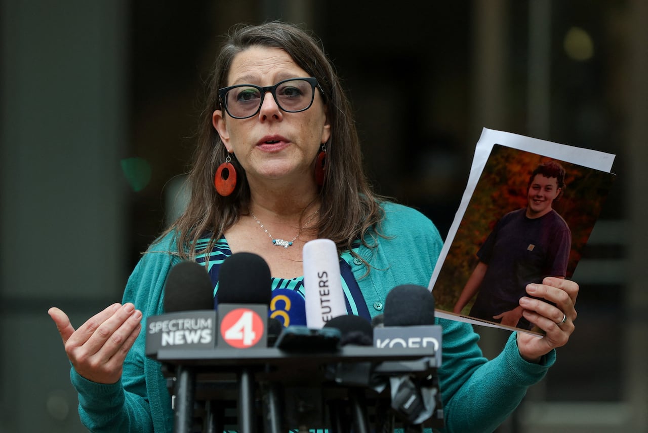 Woman with dark hair and glasses holds a photo as she speaks at a podium