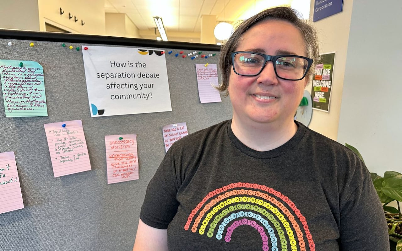 A woman wearing a rainbow t-shirt stands in front of a tack board that reads "How is the separation debate affecting your community."