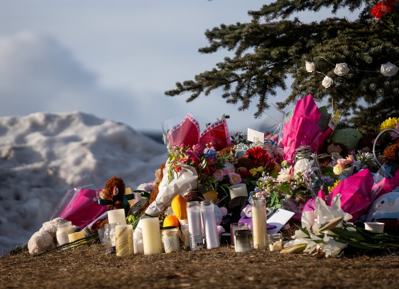 Flowers, candles and ornaments are seen at the base of a snowbank.
