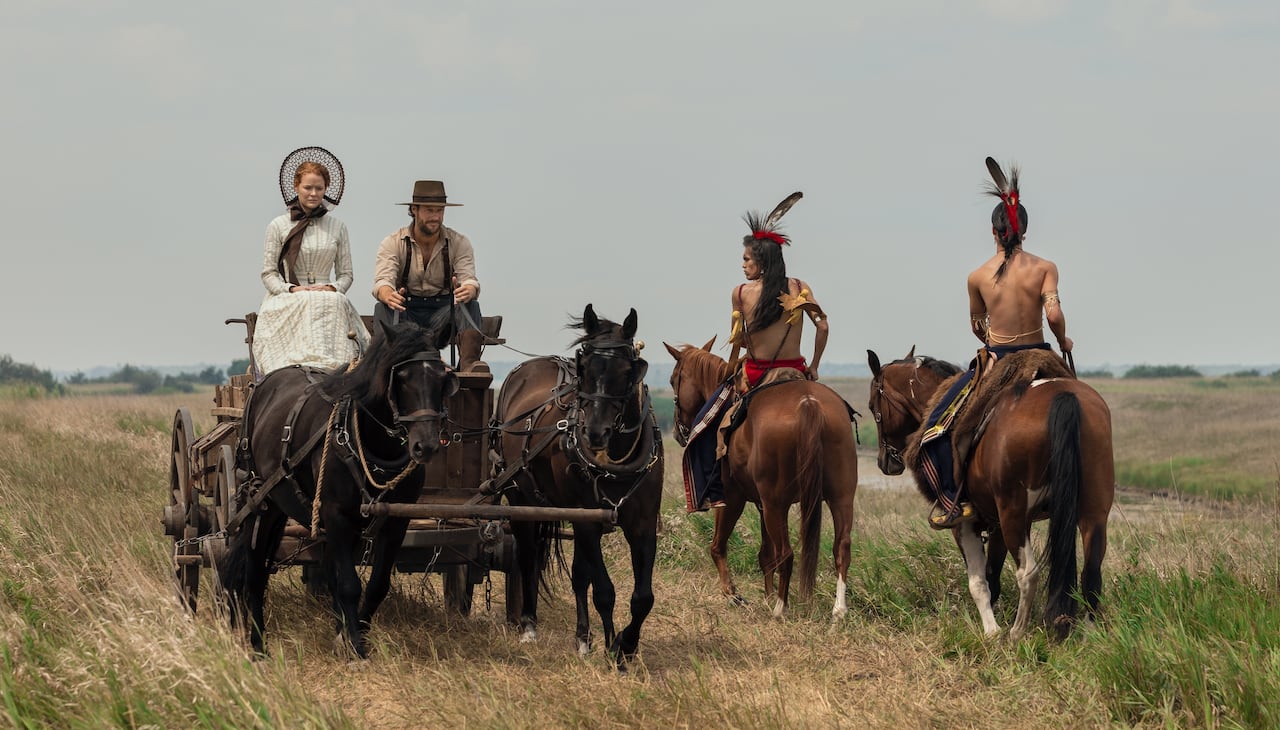 Pioneers riding in a wagon past two Osage men on horseback.