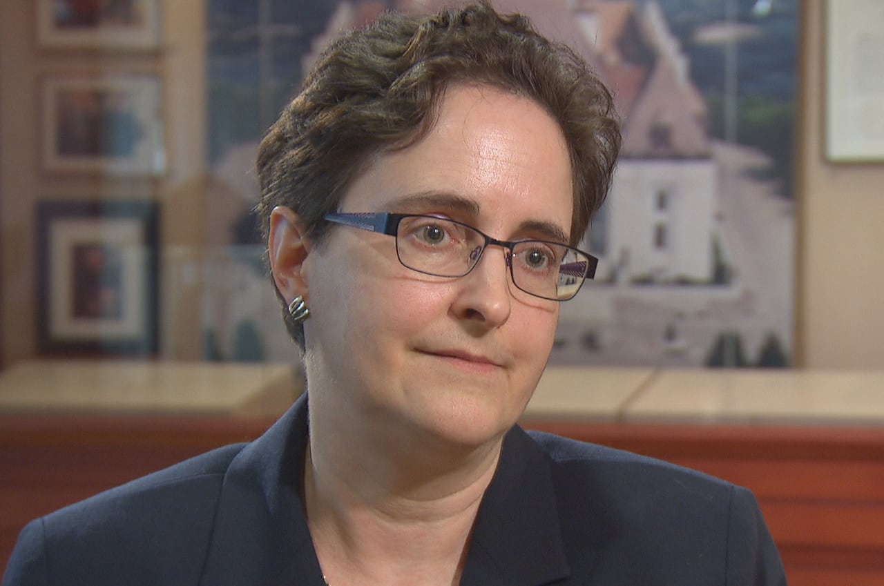 A woman with short hair and glasses wearing a dark blazer.