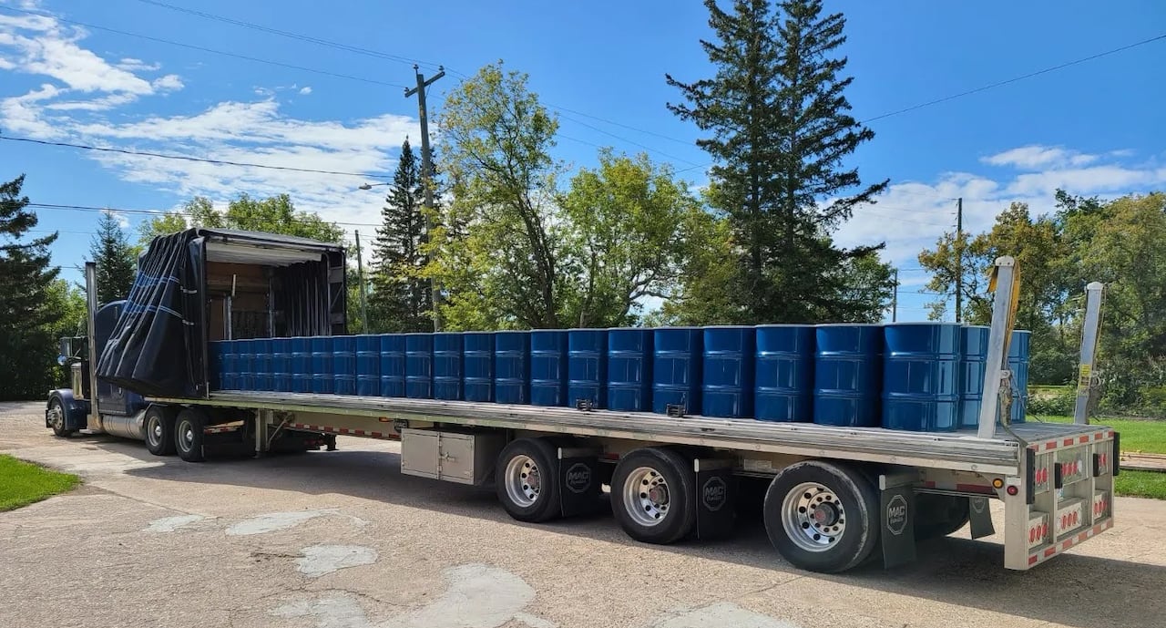 A transport truck's flatbed is filled with blue barrels
