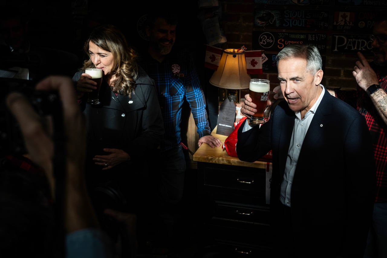 A woman and a man in a darkened room sip from glasses of beer