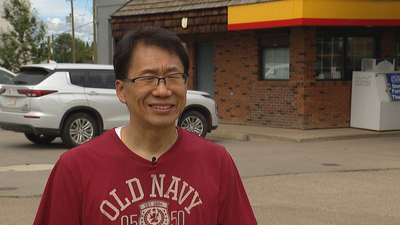 一名东亚裔男子身着红色T恤站在邻里小店前