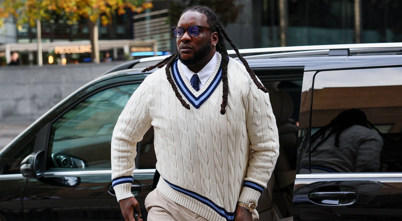 A man in a white sweater steps out of a black van.